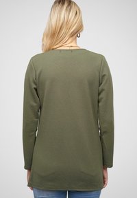 Olive green long-sleeve top, featuring a textured ribbed design, round neckline, and a relaxed fit, with a curved hem and stitched accents.