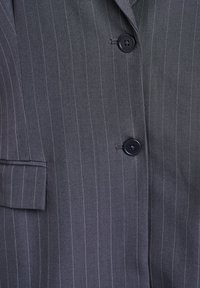 Blazer gris con rayas en relieve que cuenta con un solo bolsillo y botones negros. Fabricado con un tejido suave y texturizado, con un ajuste entallado.