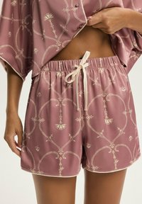Krótkie jedwabne szorty w kolorze zakurzonego różu z geometrycznym kremowym wzorem. Elastyczny pas ze sznurkiem do regulacji i dekoracyjnym wykończeniem u dołu.