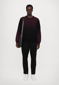 Pulover bărbați cu gradient de la burgundy închis la negru, cu mâneci lungi, asortat cu pantaloni negri și adidași albi, purtând o geantă de umăr neagră.