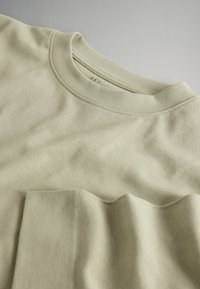 Hellgrünes Baumwoll-T-Shirt mit Rundhalsausschnitt und Brusttasche. Es zeichnet sich durch eine glatte Stoffstruktur und dezente Nähte aus.