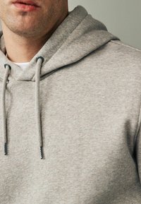 Sudadera gris claro con una textura suave, que cuenta con capucha ajustable. La tela es suave y casual, con un corte holgado.