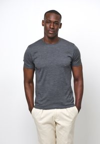 Grå kortärmad t-shirt i ett mjukt, strukturerat material; tillsammans med ljusbeiga byxor, stående mot en helt vit bakgrund.