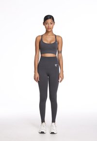 Szary sportowy crop top i legginsy z wysokim stanem, charakteryzujące się gładką teksturą i subtelnym detalem z logo, zestawione z białymi butami sportowymi.