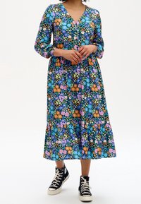 Robe maxi à motifs floraux avec un décolleté en V, des manches longues et un ourlet à volants, présentant des couleurs comme le bleu, l'orange et le rose sur un fond sombre.