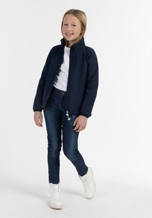 Marineblauwe zip-up jas van een zacht materiaal, gecombineerd met een wit T-shirt, donkerblauwe jeans en witte sneakers. Ontspannen pasvorm, eenvoudig design.