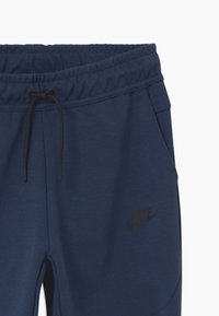 Marinblå sweatpants med elastisk midja, snörning, sidofickor och en svart Nike-logotyp på underbenet. Mjuk tygkvalitet.