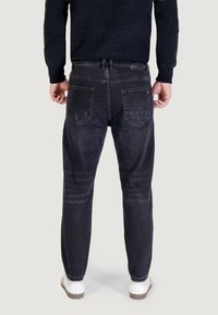 Jeans in denim scuro con vestibilità dritta, caratterizzati da una texture sbiadita, tasche posteriori classiche e un leggero aspetto usurato. Abbinati a sneakers bianche.