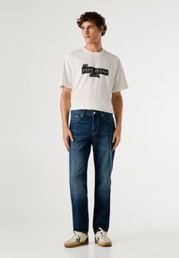 Bílé tričko s černou grafikou "Pepe Jeans London", spárované s tmavě modrými džíny rovného střihu a světlými teniskami.