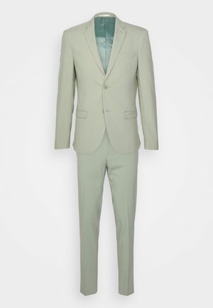 Lichtgroen pak met een op maat gemaakte jas die een enkele knoop en notch-revers heeft, gecombineerd met slim fit broeken. Gladde stoftextuur.