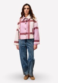 Gebreide cropped jack in lichtroze met rijke rode strepen, met een brede kraag, knopen en zijzakken. Gepaard met high-waisted jeans.