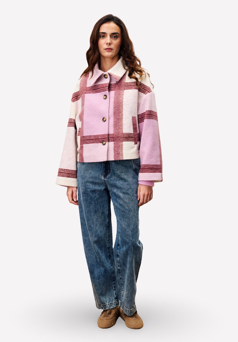 Gebreide cropped jack in lichtroze met rijke rode strepen, met een brede kraag, knopen en zijzakken. Gepaard met high-waisted jeans.