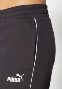 Calções atléticos pretos feitos de tecido suave, com uma risca vertical branca de cada lado e um logo branco da Puma perto da bainha.