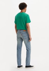 Camiseta de algodón verde con un corte relajado, combinada con unos vaqueros de pierna recta en azul claro con un parche de cuero y bolsillos traseros. Zapatillas negras.