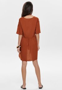 Rostbraunes Kleid mit kurzen Ärmeln, Rundhalsausschnitt, elastischem Bund und knielanger Saumlänge; hergestellt aus leichtem, fließendem Stoff.