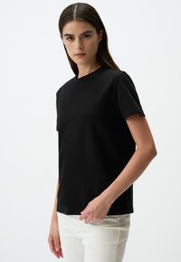 Zwarte katoenen t-shirt met een ronde hals en korte mouwen, met een rechte snit en zachte textuur, gecombineerd met witte slim-fit broek.