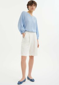 Hellblaue, langärmelige Bluse mit Knopfleiste, kombiniert mit weißen gestreiften Shorts und blauen Ballerinas. Glattes Material mit elastischen Bündchen.