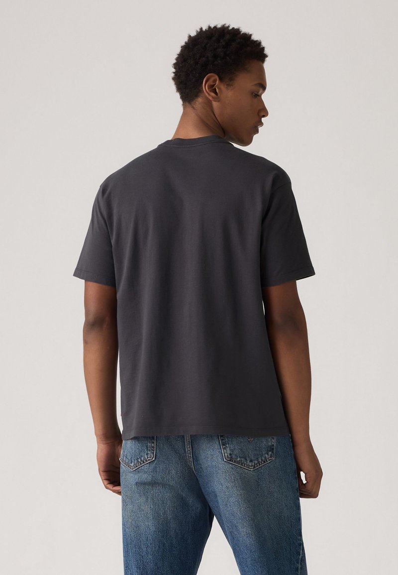 Dunkelgraues Baumwoll-T-Shirt mit kurzen Ärmeln, ausgestattet mit einem klassischen Rundhalsausschnitt und einer lässigen Passform, kombiniert mit hellblauen Jeans.