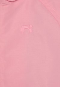 Tessuto per abbigliamento rosa chiaro con un logo cucito in modo sottile a forma di "n" minuscola, caratterizzato da una trama liscia e linee pulite.