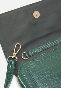 Interno di una borsa in pelle verde con motivo coccodrillo, dotato di hardware dorato e chiusura con clip e zip; rivestimento in tessuto visibile.
