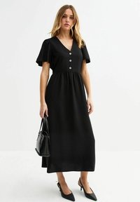 Vestido maxi negro con mangas cortas acampanadas, escote en V y detalle de tres botones en la parte delantera. Tejido suave y corte relajado.