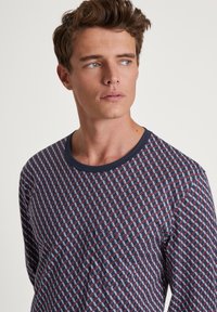 Chemise à manches longues avec une base bleu marine et un motif géométrique rouge et blanc. Coupe confortable, col rond et texture de tissu douce.