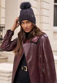 Kötött tengerészkék sapka műszőrme bojttal; bordó krokodilmintás bőrkabát kétsoros gombolással, alatta texturált fekete pulóver.