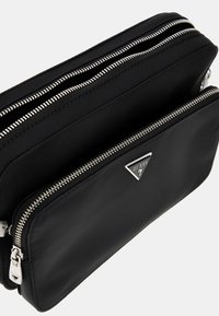 Black nylon clutch with two zippered compartments, silver hardware, and a triangular logo accent. Smooth texture with a sleek design.