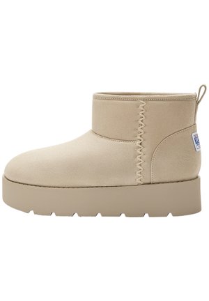Beige ankelstøvle med tyk, flad sål, zigzag-syning i siden, trækflap ved hælen og et lille logopatch på bagsiden.
