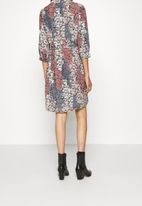 Blommönstrad klänning med trekvartslånga ärmar, åtsittande midja och knälängd. Färgerna inkluderar blå, rosa och röd med ett vitt blommönster.