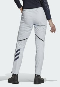 Pantalones deportivos de color gris claro con un ajuste tapered, que presentan detalles en negro y bolsillos diagonales con cierre, fabricados con un material suave y ligero.