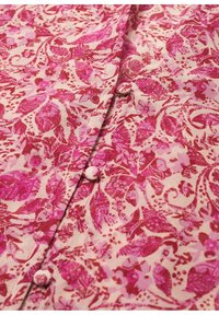 Blusa floral rosa con fondo crema, que presenta patrones intrincados de hojas y flores, y cierres de botones a lo largo de la línea frontal.