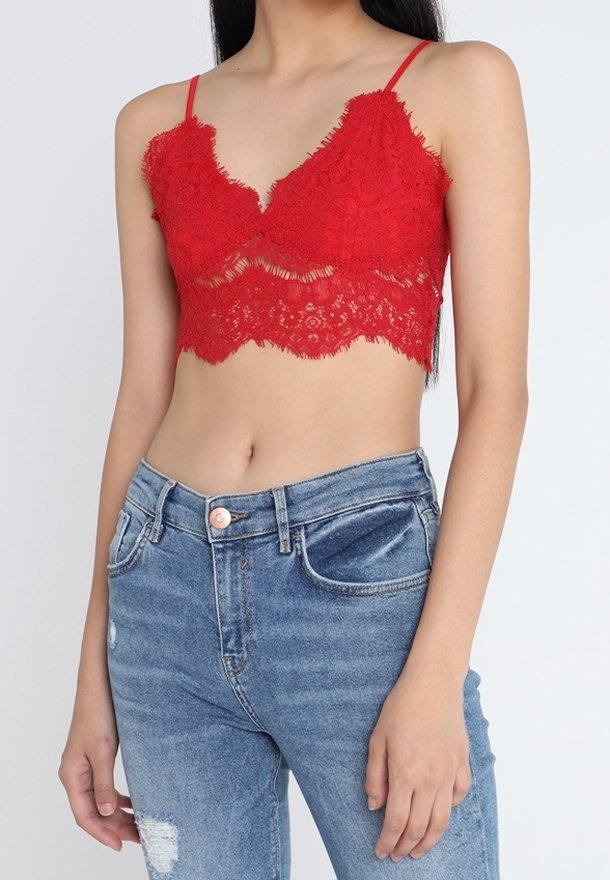Bralette en dentelle rouge avec bretelles réglables, doté d'un ourlet festonné et d'une texture transparente, associé à un jean bleu clair déchiré.
