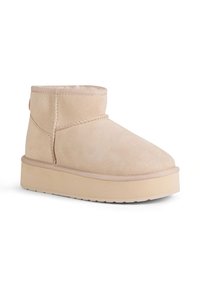 Beżowy zamszowy botek za kostkę z okrągłym noskiem, przeszywanymi detalami i grubą, podwyższoną podeszwą. Gładka faktura z minimalnymi akcentami.