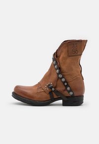 Stivale alla caviglia in pelle marrone con punta rotonda, design arricciato, borchie in metallo e cinture. Presenta un tacco impilato e dettagli cuciti.