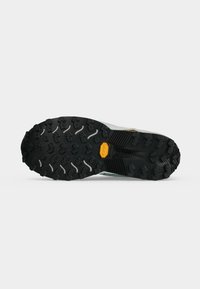 Schwarze robuste Schuhsohle mit tiefem Profil für guten Halt, mit einem gelben Vibram-Logo nahe der Mitte auf weißem Hintergrund.
