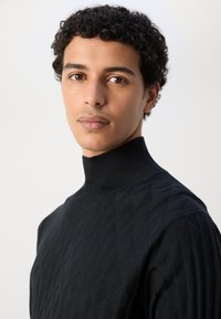 Schwarzer Rollkragenpullover mit strukturiertem Rautenmuster und geripptem Kragen. Verfügt über ein tailliertes Design und glattes Strickmaterial.