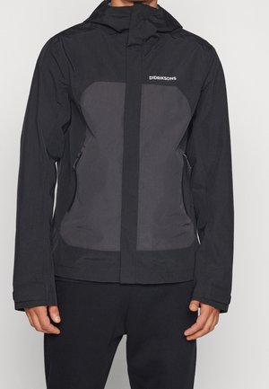 Man draagt een zwarte en donkergrijze Didriksons capuchontrui met ritssluitingen aan de zakken en lange mouwen, staand tegen een effen achtergrond.