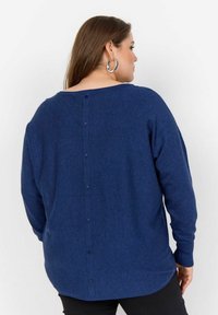 Granatowy sweter dzianinowy o luźnym kroju, z okrągłym dekoltem, długimi rękawami oraz zapięciem na guziki z tyłu wzdłuż kręgosłupa. Miękka faktura.