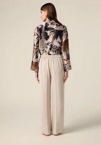 Blusa a fiori in beige, nero e tonalità di rosso, abbinata a pantaloni larghi beige con vita elastica.
