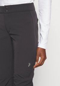 Zwarte, rekbare broeken met een hoge taille, zijzakken, twee knopen bij de taille en een metallic logo op het onderste deel van het linkerpantalon.