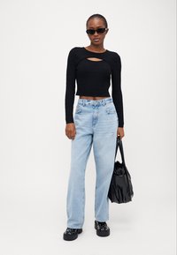 Musthave mustradaga mustkudumine cropped top läbilõikega, helesinised sirged teksad, mustad platvormkingad ja läikiv must kott.