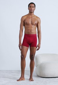 Κόκκινα αντρικά εσώρουχα τύπου μποξεράκι με υφή, με μαύρη ζώνη στη μέση που φέρει την ένδειξη "BJÖRN BORG." Το υλικό φαίνεται λείο και εφαρμοστό.