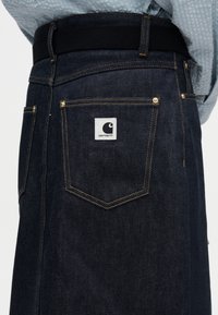 Σκούρο τζιν φόρεμα με ίσια γραμμή, αντίθετη κίτρινη ραφή, τέσσερις τσέπες και λευκή ετικέτα λογότυπου στο πίσω μέρος. Μαύρη μέση.