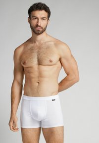 Vita bomullboxer med en åtsittande design, elastiskt midjeband och en centrerad frontficka. Slät struktur och minimal varumärkesdetalj.