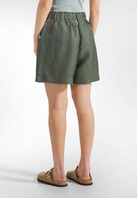 Pantaloncini verdi in lino con vita arricciata, tasche laterali e orlo risvoltato. Abbinati a sandali piatti marrone chiaro.