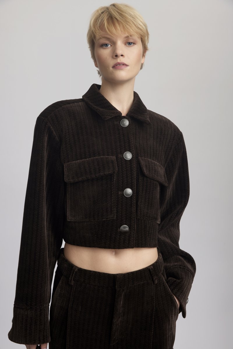 Chaqueta de pana marrón cortada con dos bolsillos фронтales, botones plateados y un cuello con solapa. Tejido texturizado con acanalado vertical.