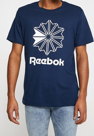 Granatowy bawełniany t-shirt z białym geometrycznym wzorem gwiazdy i logo "Reebok" w pogrubionej czcionce na wysokości klatki piersiowej. Krótkie rękawy, luźny krój.