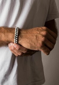 Mustvalge helmesriba, millel on vahelduvad spheroid- ja tsilindrilised kujundid, kantud randmel, näidates tekstuurset ja elastset disaini.