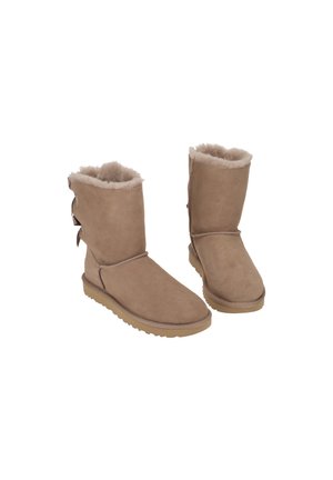 Bottes d'hiver mi-mollet couleur beige avec doublure en laine douce et trois nœuds décoratifs à l'arrière, semelles plates en caoutchouc, présentées sur fond blanc.